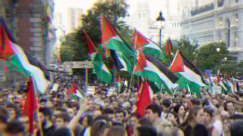 A large pro-Palestine protest in Madrid. Hundreds of people are gathered in the street with dozens of Palestinian flags visible.