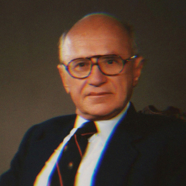 A portrait of Milton Friedman. He wears thick, round glasses, a blue suit jacket and red and black striped tie.