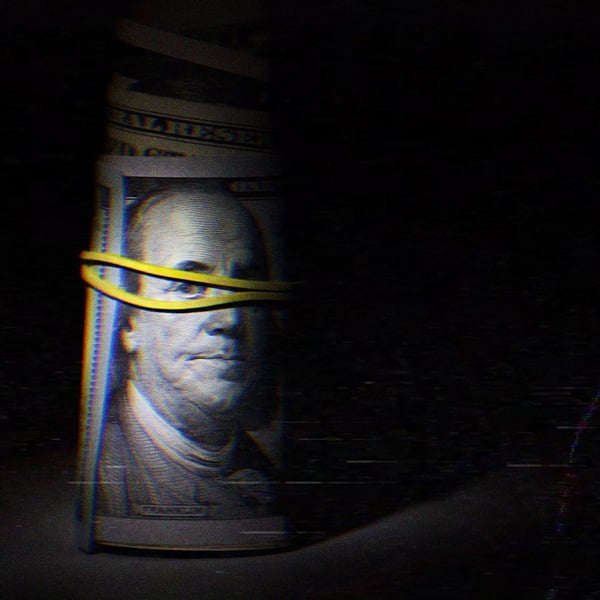 A roll of cash tied with a rubber band; a $100 bill is visible on the outside.