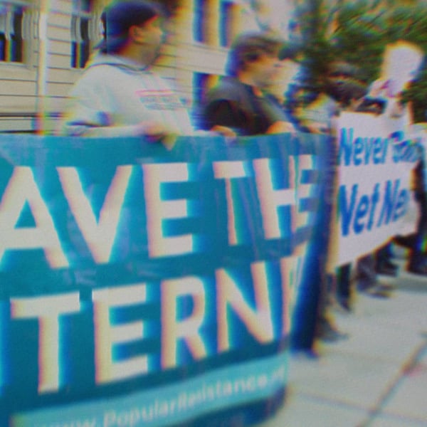 Activists at a net neutrality protest holding signs that say Save The Internet and Never Gonna Give Up Net Neutrality.