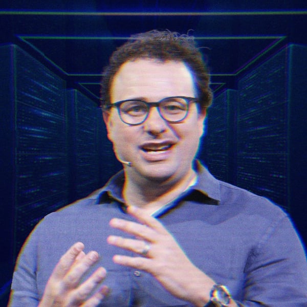 Dario Amodei mid-speech, hes wearing a wireless mic and is talking with his hands. His image is overlayed over a rendering of futuristic server room.