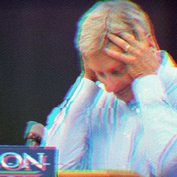 Gary Johnson standing at a podium, resting his elbows on the surface with his hands on his head.