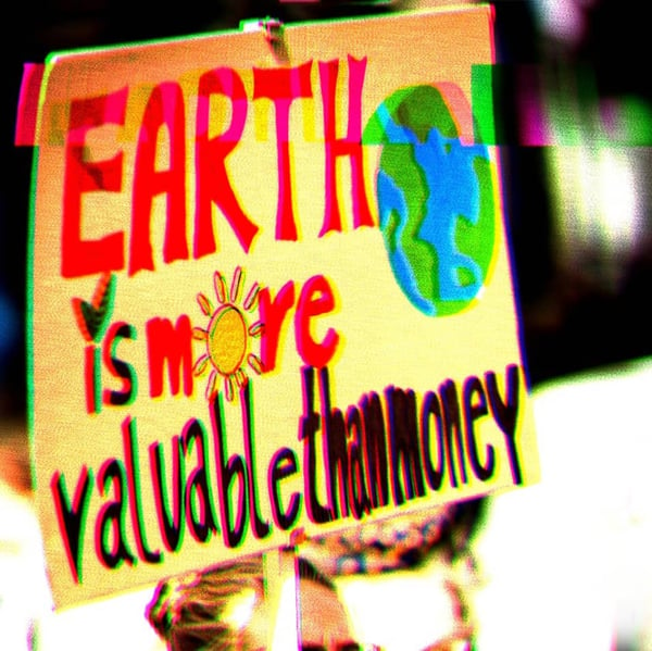 Protest sign that says, “Earth is more valuable than money,” with a drawing of the earth.