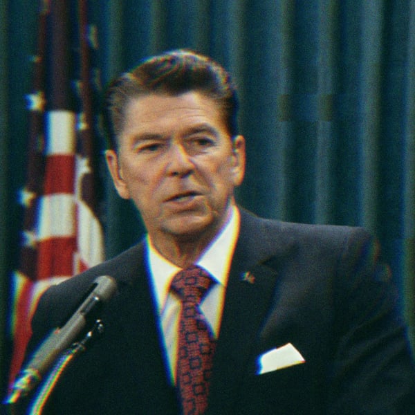 Ronald Reagan standing at a podium, speaking. An American Flag is visible behind him.