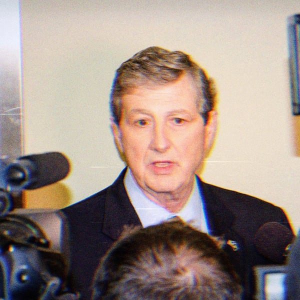 Senator John Kennedy speaking at a press conference. There are cameras and microphones in his face and he has a goofy expression on his face.