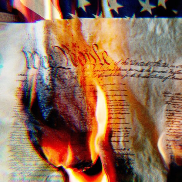 The U.S. Constitution on fire, the words We The People are burning. The U.S. flag is slightly visible in the background.