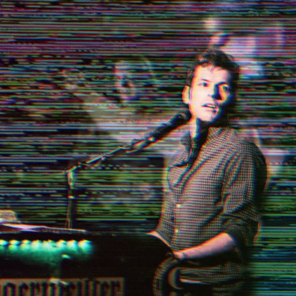 Tom McGovern Sitting at a piano and microphone with a glitchy static background