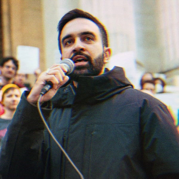 Zohran speaking into a microphone at a rally.