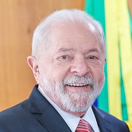 Lula smiling wearing a suit and tie. He has short white hair and a beard