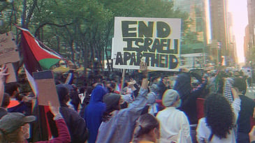 A large group of protesters gathering in NYC. The Palestinian flag is visible, as well as a sign that reads ‘End Israeli Apartheid.’