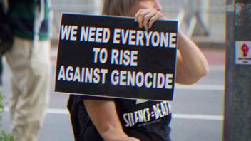 A person holding a sign that says 'We need everyone to rise against genocide.' 