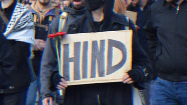 A protester holding a red flower and a sign that simply reads, ‘HIND.’