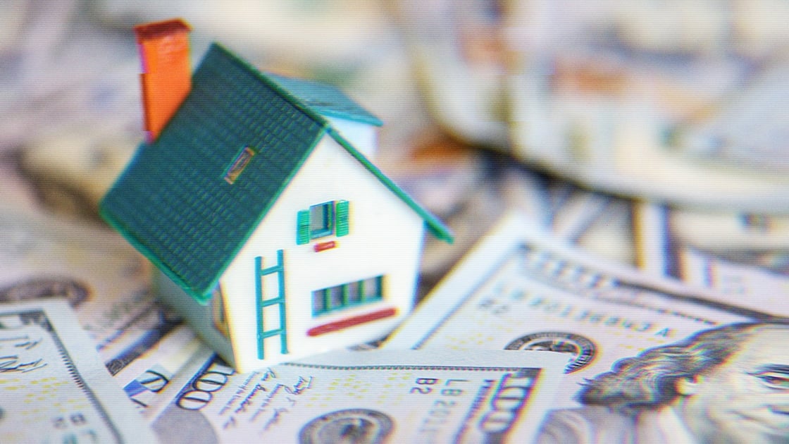 A toy house surrounded by $100 bills.