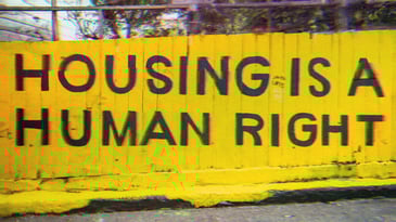 A yellow wall with bold black text that reads ‘Housing Is A Human Right.’