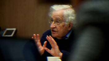 Noam Chomsky speaking, his hands raised.