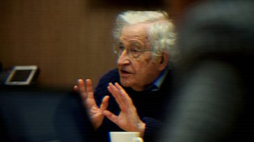 Noam Chomsky speaking, his hands raised.