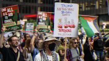 People protesting for Palestine. A person carries a sign that says, ‘Trump, Netanyahu, Biden Harris: Butchers of Palestine.’ Another sign reads, ‘End All U.S. Aid to Israel.’ Palestinian flags are flown in conjunction with the signs.