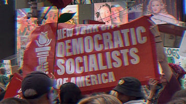 Rally in Times Square, NYC. Individuals are holding up a red banner that reads ‘New York City Democratic Socialists of America.’