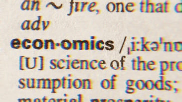 The definition of economics in the dictionary. Visible text reads [U] science of the pro...sumption of goods; material prosperity.