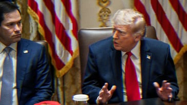 Trump speaking, gesturing with his hands at a cabinet meeting. Marco Rubio is seated beside him.