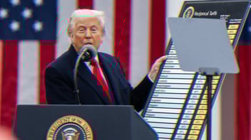 Trump standing at a podium speaking into a microphone holding a poster titled Reciprocal Tariffs.