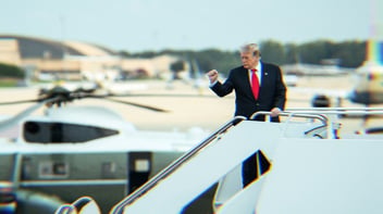 Trump standing on airplane stairs facing forward raising his fist in the air.
