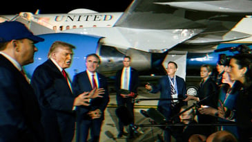 Trump talking to reporters before he boards Air Force One, visible in the background.