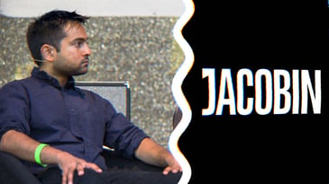 A photo of Bhaskar Sunkara sitting on the stage, next to the Jacobin logo
