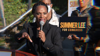 Summer Lee speaking at an event with signs behind her that say Summer Lee for Congress.