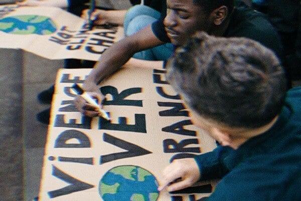 Two people making a protest sign for climate change that says evidence over ignorance