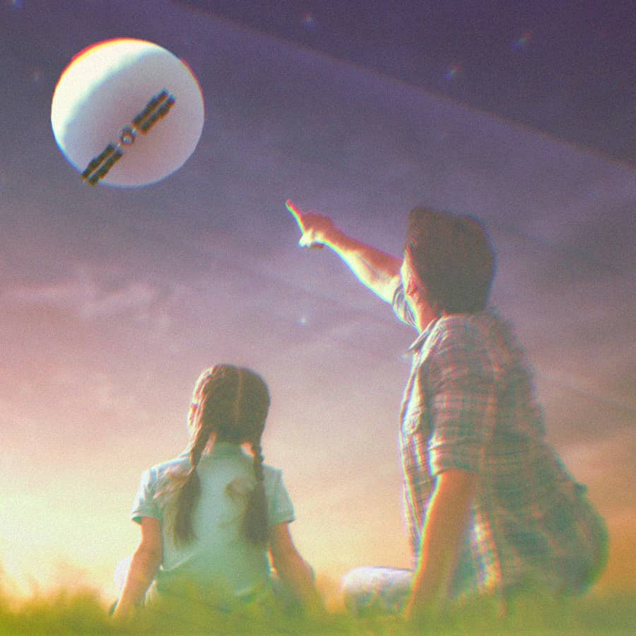 A father and daughter sitting on the grass at night. The dad is pointing at the spy balloon in the sky.
