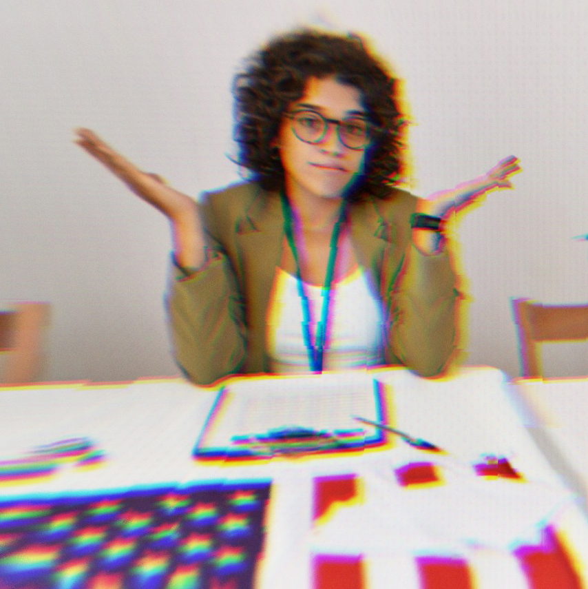 A person sitting in front of an American flag at a polling check in table shrugging, confused.