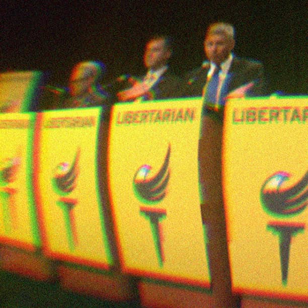 Candidates standing at yellow podiums that have the Libertarian logo on them.