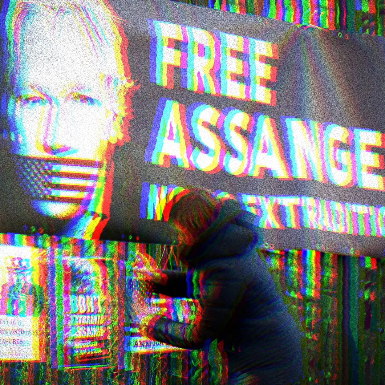 Glitchy photo of a banner with a photo of Julian Assange with American Flag tape over his mouth. Banner text says, ‘Free Assange. No U.S. Extradition.’ Below the banner a woman is adding another pro-Assange poster.