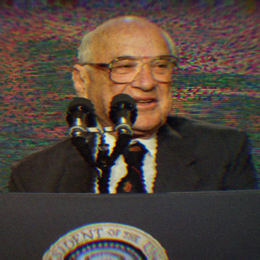Milton Friedman speaking at a podium; the background is a glitchy rainbow.