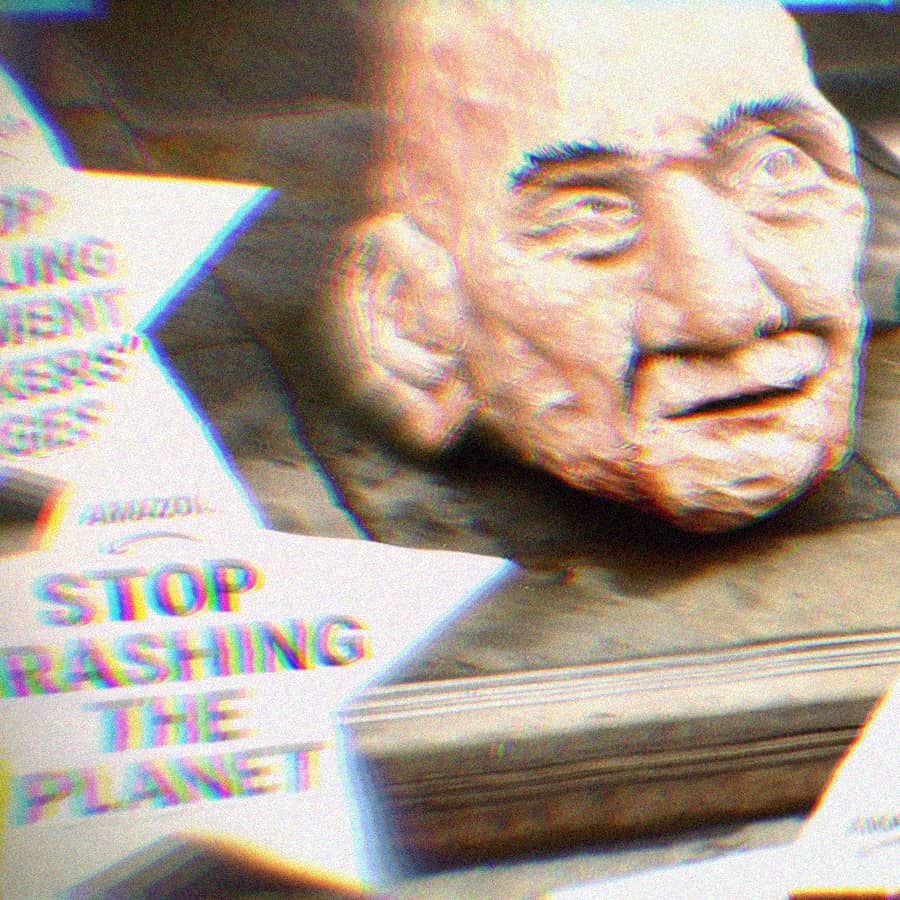 Paper Mache head of Jeffrey Bezos surrounded by protest signs that say 'Stop Trashing The Planet' 'Stop Injuring Workers' 'Stop Spying on Workers' and 'Stop Stealing Garment Workers Wages.'