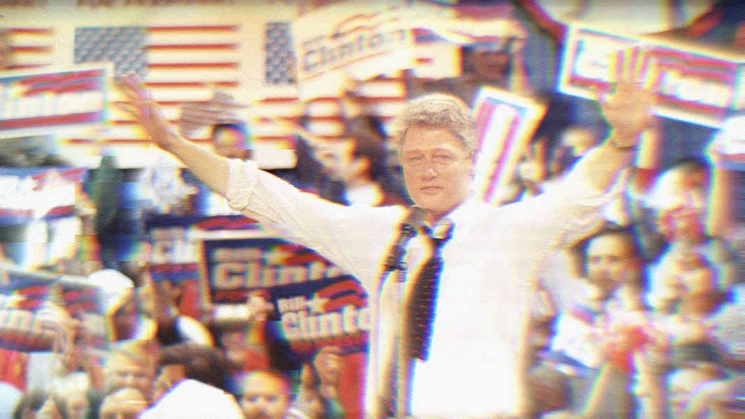 Bill Clinton on the campaign trail in 1992. He's speaking into a microphone, as the crowd behind him holds 'Bill Clinton' signs.