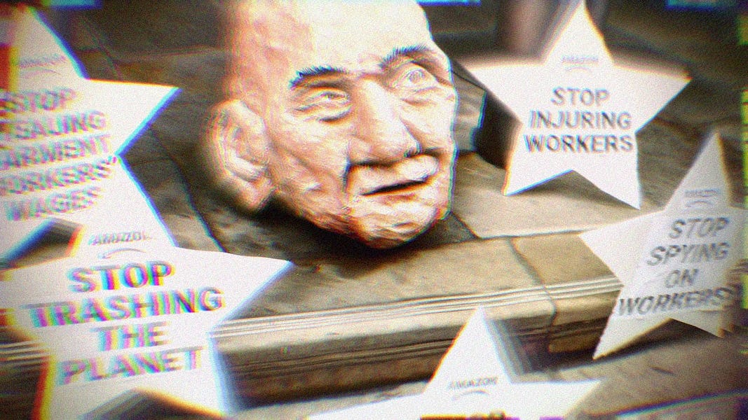 Paper mache head of Jeffrey Bezos, surrounded by protest signs that say, 