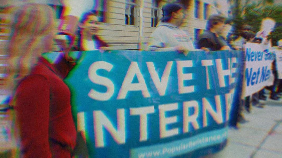 Activists at a net neutrality protest holding signs that say 'Save The Internet' and 'Never Gonna Give Up Net Neutrality.'