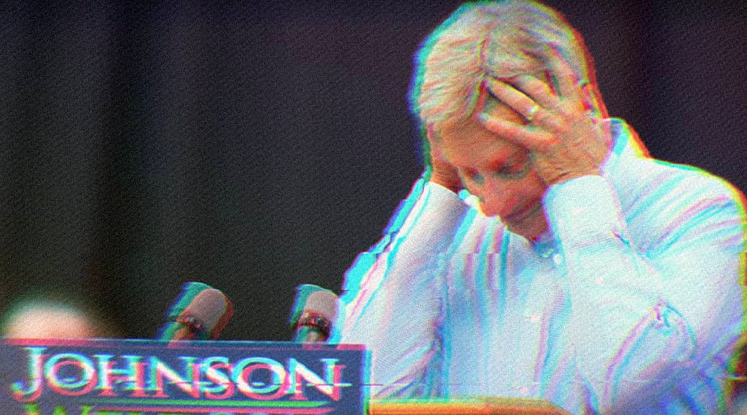 Gary Johnson standing at a podium, resting his elbows on the surface with his hands on his head.