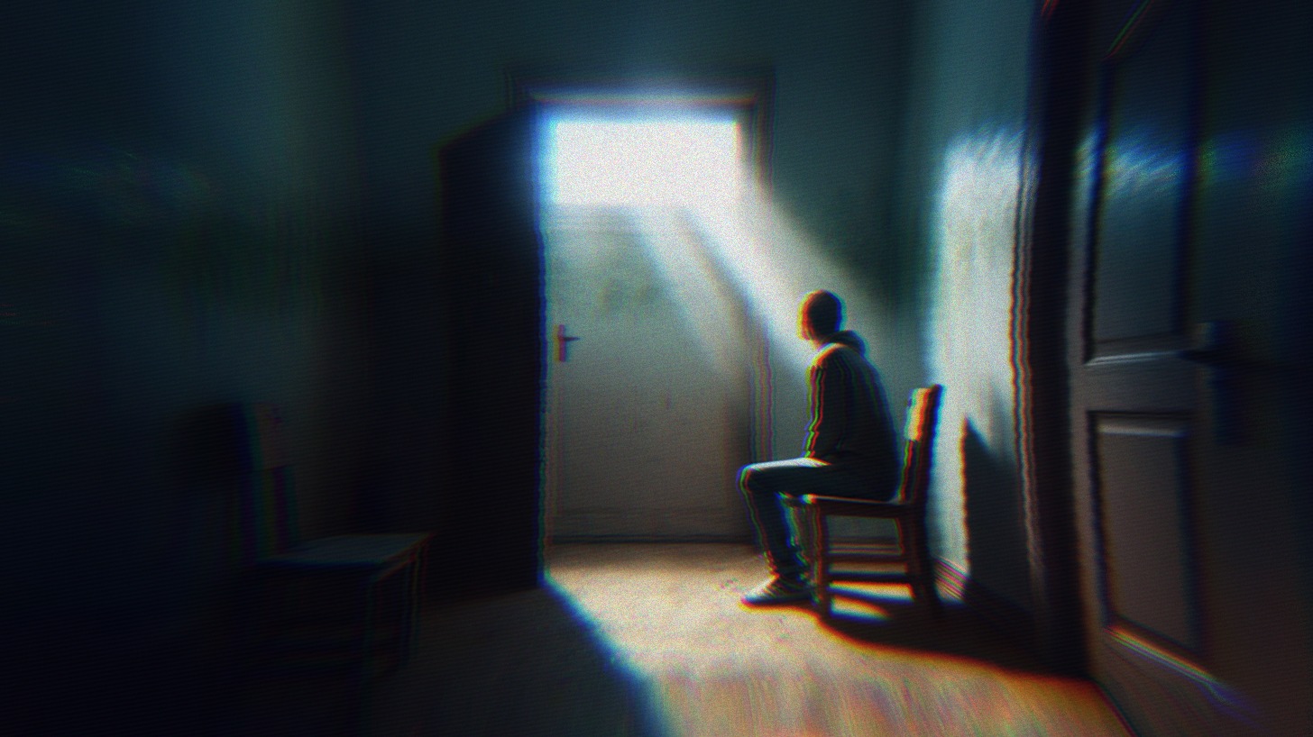 A person sitting on a chair in the dark with light coming through the window.