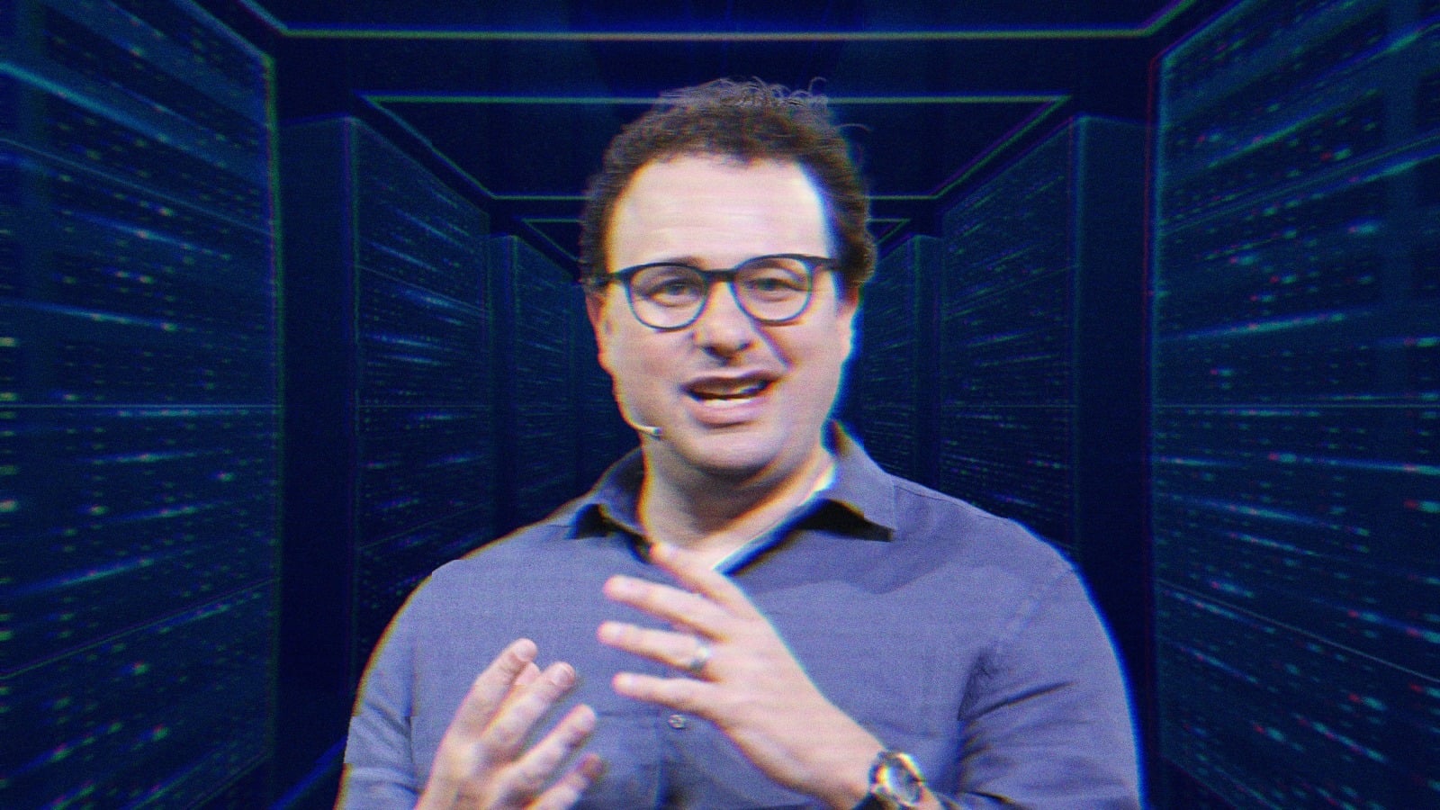 Dario Amodei mid-speech, he's wearing a wireless mic and is talking with his hands. His image is overlayed over a rendering of futuristic server room.