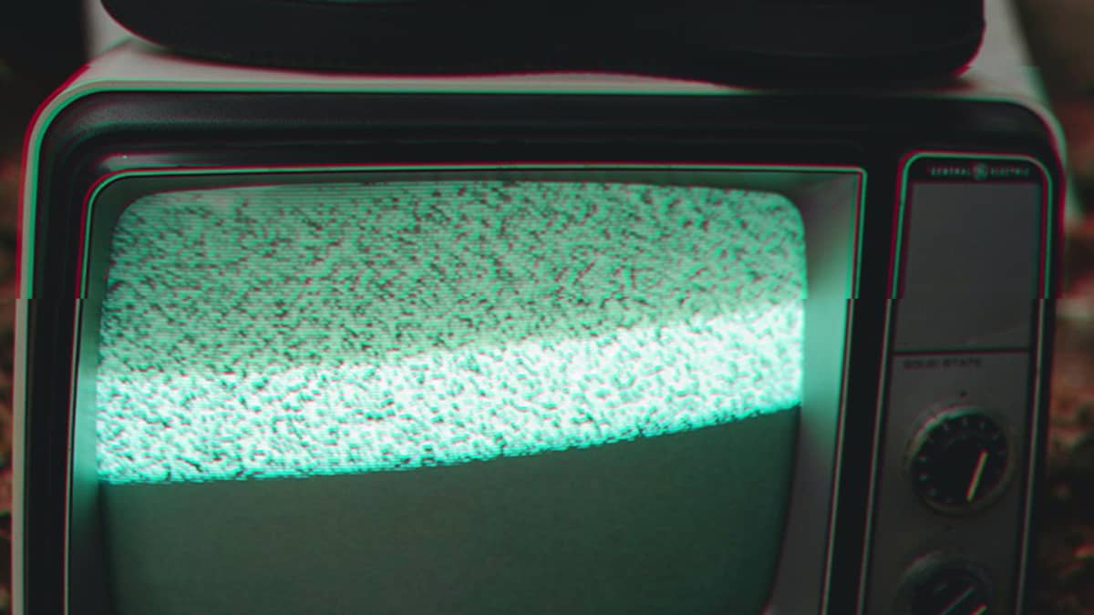 A person has their foot on an old tv set; the screen shows green, white and black static.