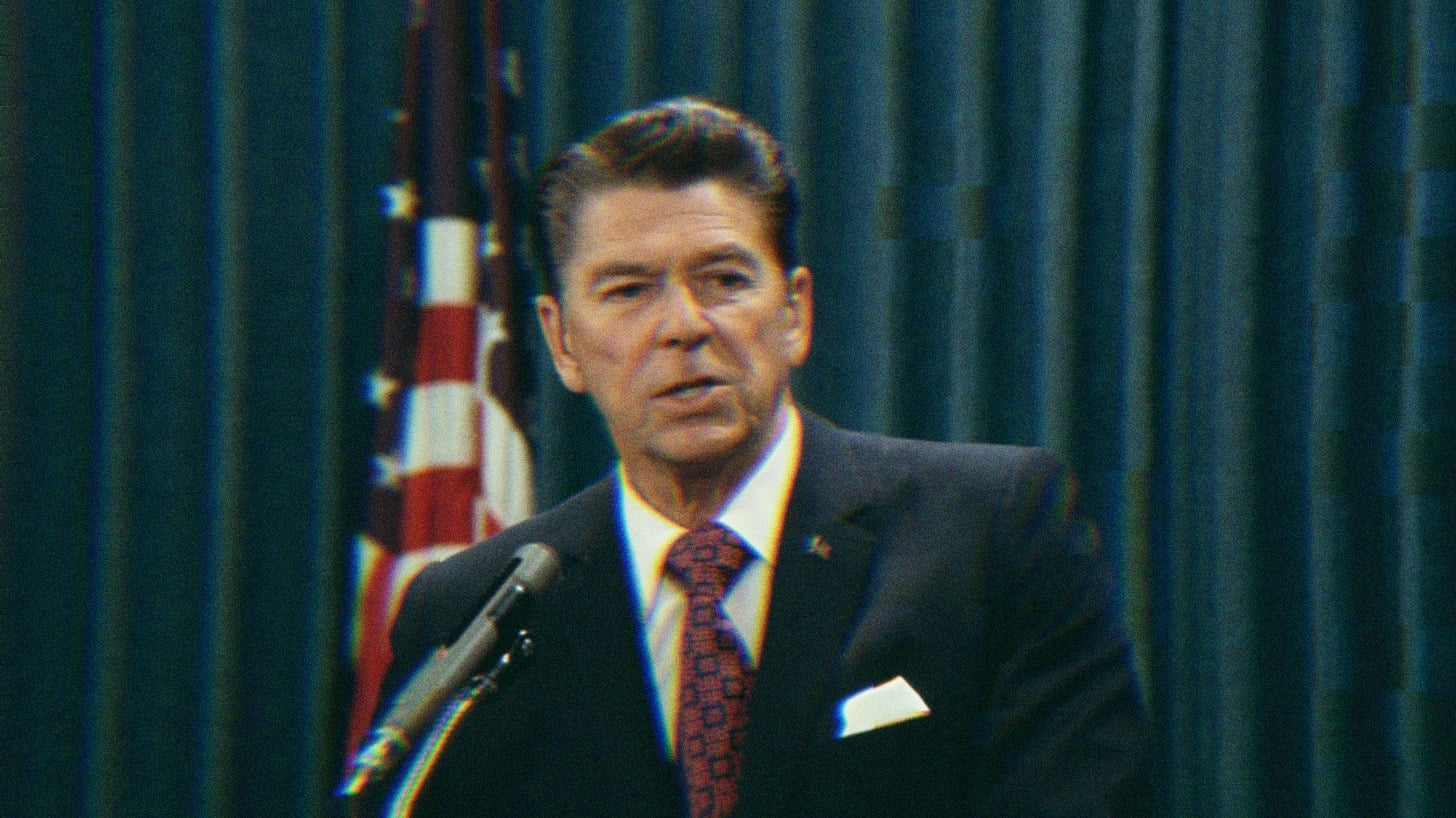 Ronald Reagan standing at a podium, speaking. An American Flag is visible behind him.