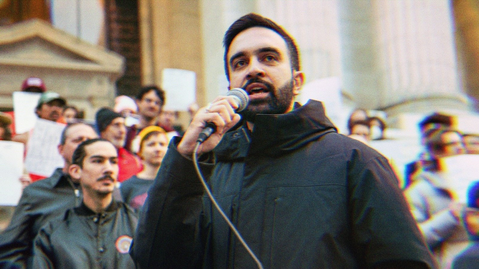 Zohran speaking into a microphone at a rally.