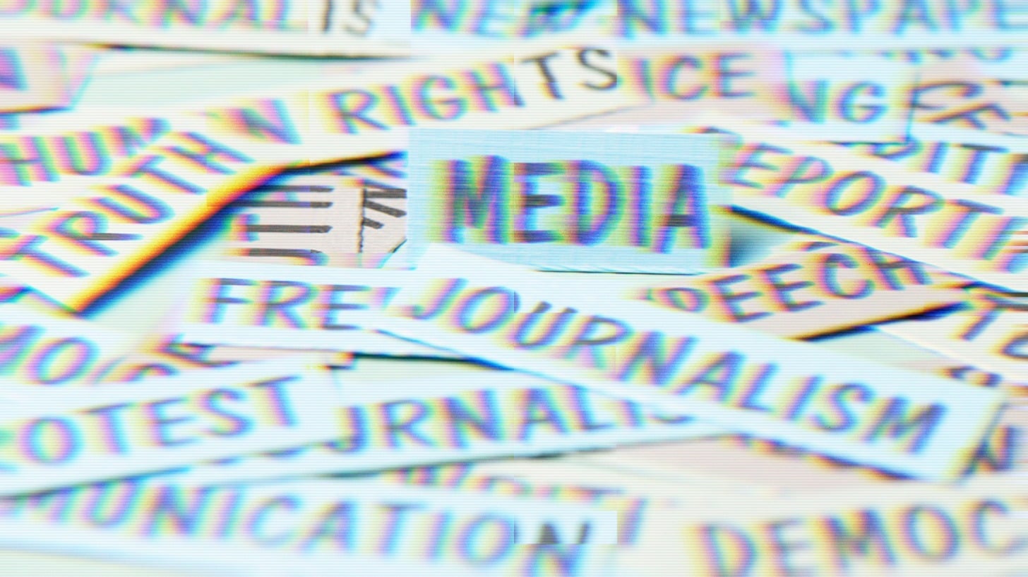 A pile of paper strips bearing words associated with press freedom and civic life, including “Media,” “Journalism,” “Truth,” “Rights,” “Free,” “Speech,” “Protest,” “Democracy,” “Newspaper,” “Reporting,” and “Communication,” with the word “Media” centered on a small card in the foreground.