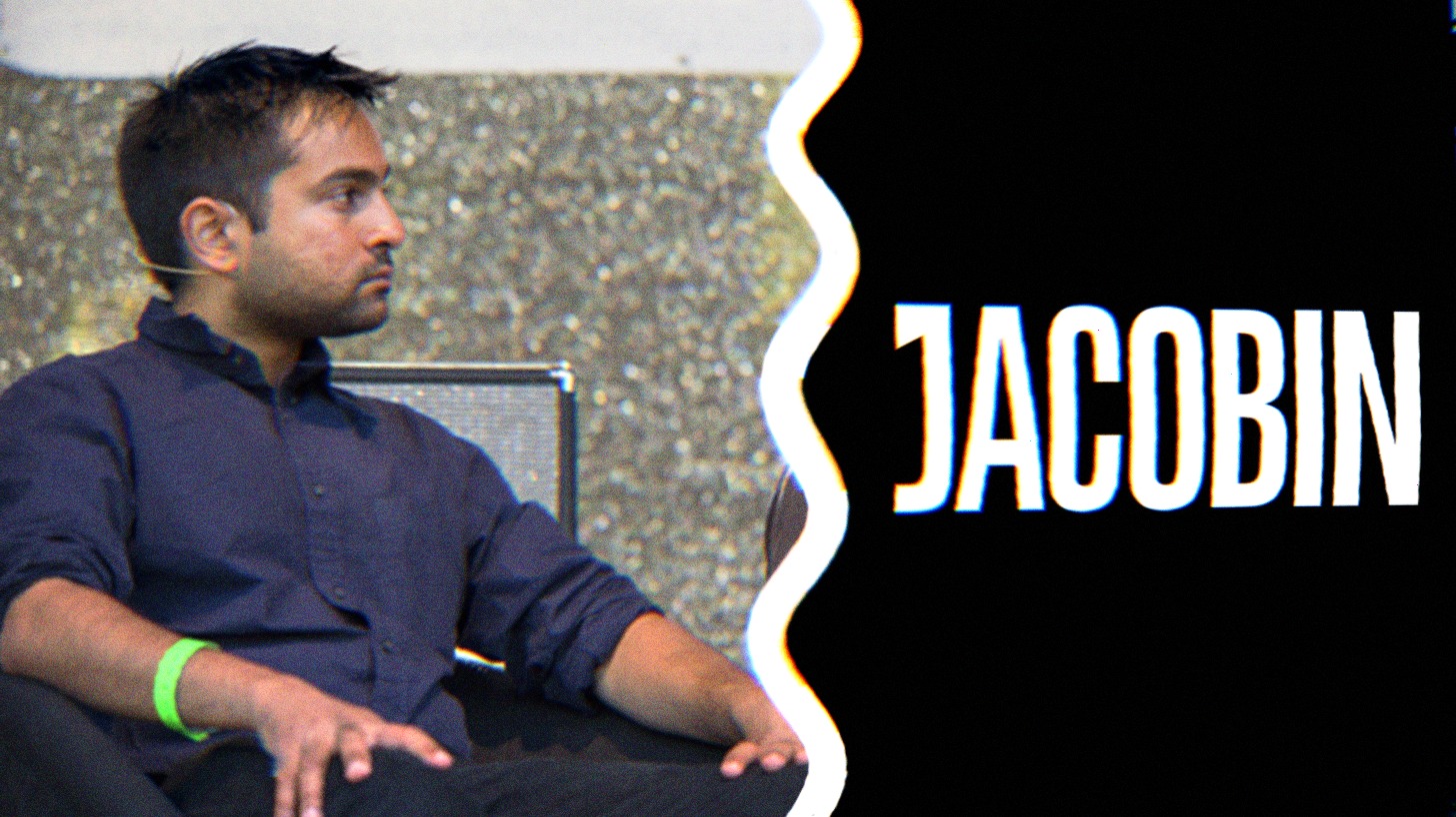 A photo of Bhaskar Sunkara sitting on the stage, next to the Jacobin logo